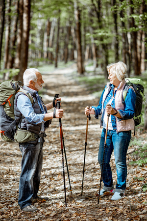 Beautiful senior couple hiking with backpacks and trekking sticks in the forest. Concept of active lifestyle on retirementの写真素材