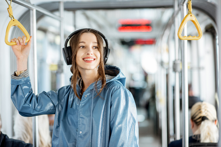 Young stylish woman enjoying trip in the public transport, standing with headphone while moving in the modern tramの写真素材