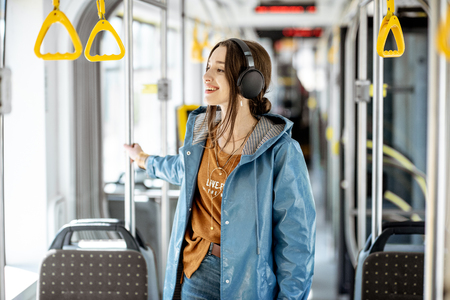 Young stylish woman with headphones while moving in the modern tram. Happy passenger enjoying trip at the public transportの写真素材