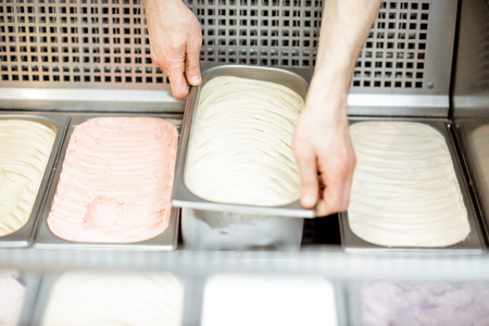 Man putting trays with ice cream into the refrigerator full of ice cream with different flavors in the shopの写真素材