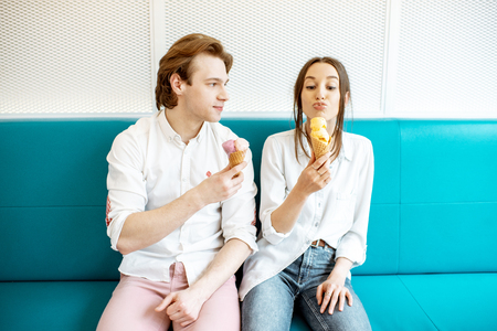 Young couple having fun, enjoying ice cream while sitting together on the bright sofa indoorsの写真素材