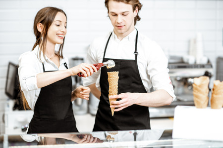 Man and woman making ice cream in waffle cones for selling, standing together at the counter of the modern shopの写真素材