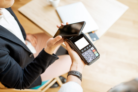 Businessman paying contactless with smart phone while sitting at the cafe, close-up viewの写真素材