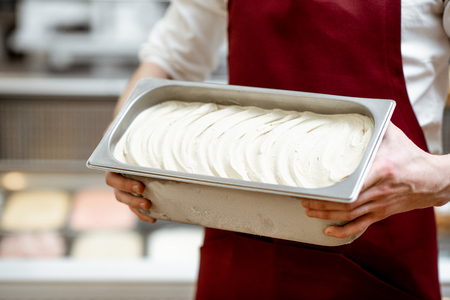 Man in red apron holding tray with ice cream for selling with shop front on the background, close-up viewの写真素材