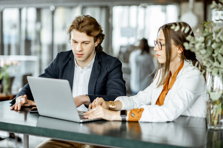 Young man and woman having a business conversation while sitting with laptop at the bar or modern...