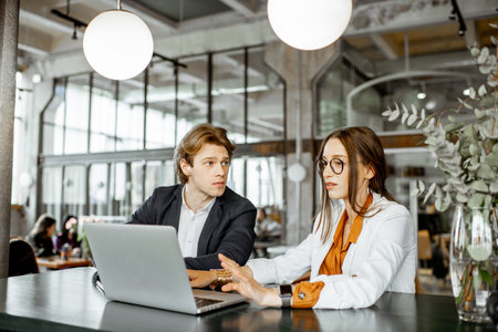 Young man and woman having a business conversation while sitting with laptop at the bar or modern...
