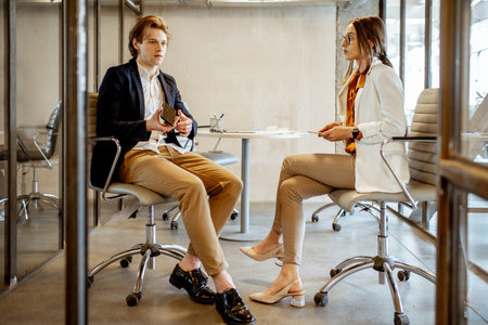 Young man and woman having a business conversation during the coffee break, sitting together in the...