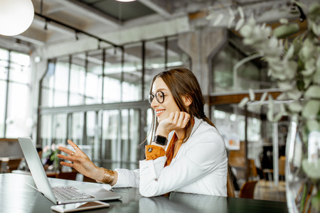 Portrait of a young and cheerful business woman sitting with laptop a the modern spacious bar or officeの写真素材