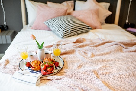 Beautiful breakfast with strawberry, buns and juice on the pink bedclothes at the bedroomの写真素材