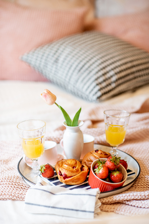 Beautiful breakfast with strawberry, buns and juice on the pink bedclothes at the bedroomの写真素材