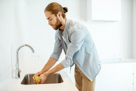 Man washing apple to eat at the modern white kitchen at homeの写真素材