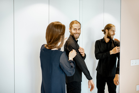 Young couple wearing black formal clothes, preparing for the serious event in the bedroom at homeの写真素材