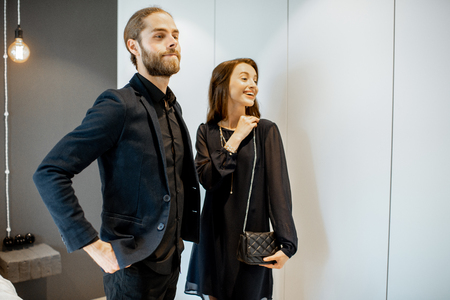 Young couple preparing for the serious event, wearing black formal clothes, standing together at the wardrobe at homeの写真素材