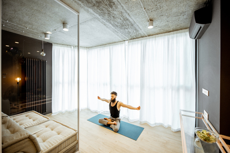 Wide view on the living room of the modern apartment with man practising yoga indoorsの写真素材