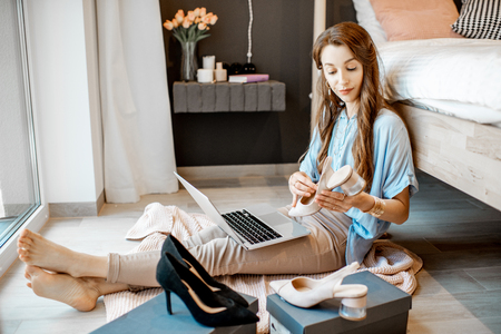 Young woman unpacking parcels with footwear, feeling happy with new online purchases, sitting in the bedroom at homeの写真素材