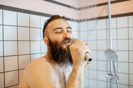 Joyful bearded man singing into the micrphone while taking a shower in the bathroomの写真素材