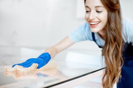 Young and cheerful housemaid wiping glass surface from the dust, cleaning at homeの写真素材