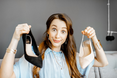 Portrait of a young woman excited with a new purchases, holding beautiful shoes while sitting on the couch at homeの写真素材
