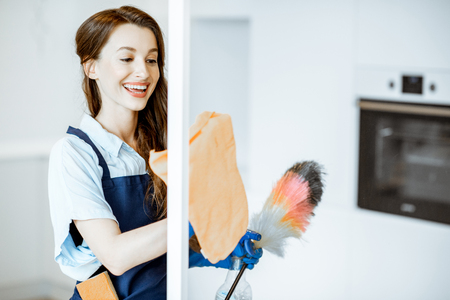 Young and cheerful housemaid wiping glass surface from the dust, cleaning at homeの写真素材