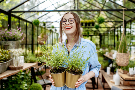 Portrait of a young woman standing with herbs at the entrance of the beautiful greenhouse or flower shopの写真素材