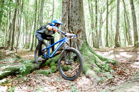 Professional well equipped cyclist riding downhill on the off road in the forest. Concept of an...