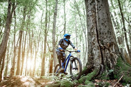 Professional well equipped cyclist riding downhill on the off road in the forest. Concept of an extreme sport and enduro cyclingの写真素材
