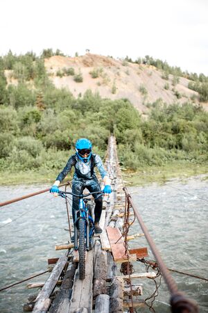 Professional well-equipped cyclist riding on the old wooden bridge in the mountains. Concept of a freeride and off road cyclingの写真素材