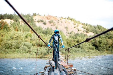 Professional well-equipped cyclist riding on the old wooden bridge in the mountains. Concept of a...