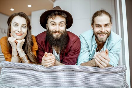 Portrait of a young and cheerful friends dressed casually sitting together on the couch at homeの写真素材