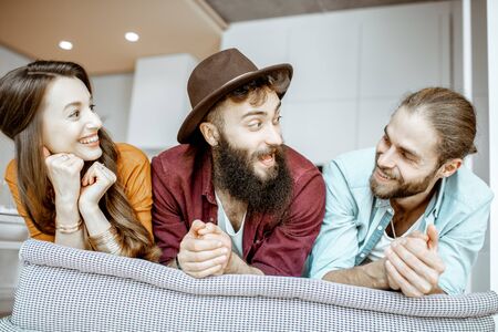 Portrait of a young and cheerful friends dressed casually sitting together on the couch at homeの写真素材