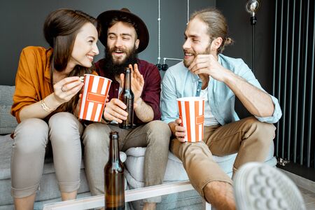 Young friends watching some movie, sitting together with pop cornes on the couch at homeの写真素材