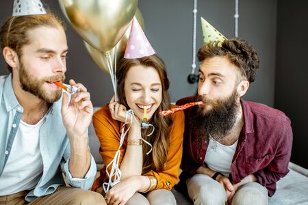 Young friends having fun with whistles during the party or birthday celebration at homeの写真素材