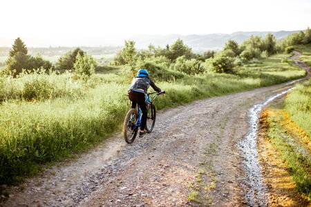 Professional well-equipped cyclist riding down on the mountain road during the sunsetの写真素材