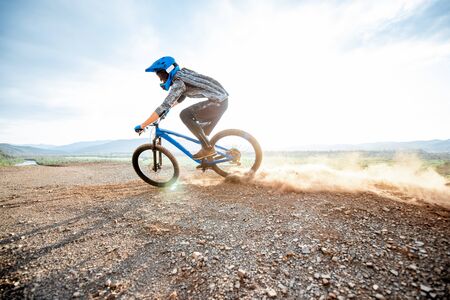 Professional well-equipped cyclist riding extremely on the rocky mountains raising dust behind during the sunsetの写真素材
