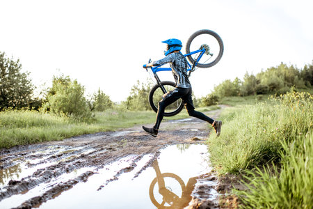 Professional well-equipped cyclist jumping through the puddle on the mountain dirt road during the...