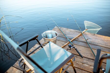 Place for fishing with fishing rods, net and bucket on the wooden pier on the lakeの写真素材