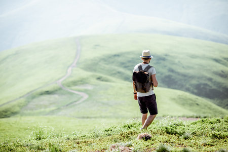Man hiking with backpack on the beautiful green meadow while traveling in the mountains during the...