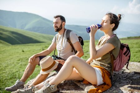Young couple drinking water while resting on the rock during the travel in the mountainsの写真素材