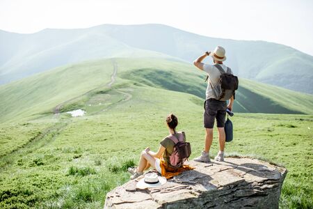 Couple enjoying beautiful landscape views, resting on the rock while traveling in the mountains during the summer timeの写真素材