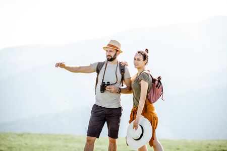 Couple enjoying beautiful views on the mountains, while traveling with backpacks in the mountains during the summer vacationsの写真素材