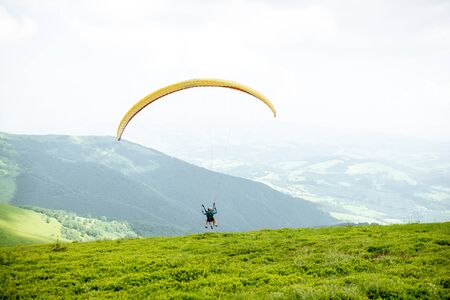 Men starting a paraglider flight, running on the green meadow high in the mountainsの写真素材