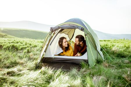 Young lovely couple in bright sweaters enjoying nature, lying in the tent while traveling high in the mountainsの写真素材