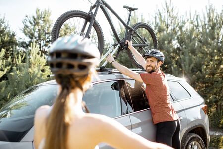 Young couple preparing for the bicycle riding, picking up mountain bicycle from the car trunk during the summer vacations in the forestの写真素材