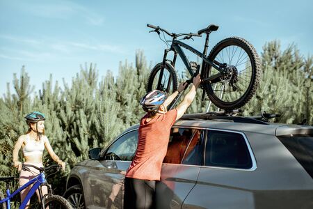 Young couple preparing for the bicycle riding, picking up mountain bicycle from the car trunk during the summer vacations in the forestの写真素材