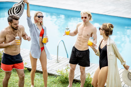 Group of happy friends having a party, dancing and drinking juice on the swimming pool during the...