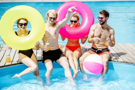 Group of a happy friends having fun, playing with inflatable balls and rings on the water pool outdoors during the summer timeの写真素材