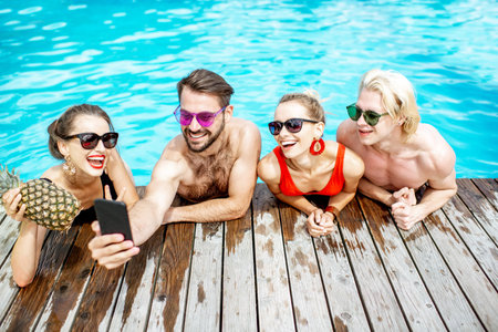 Group of a happy friends making selfie photo with phone, while having fun on the swimming pool...