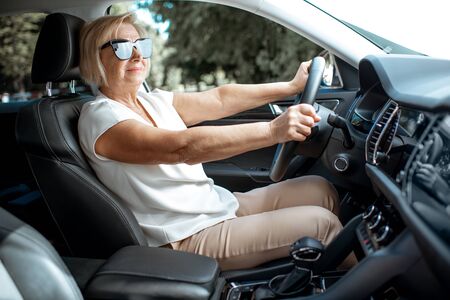 Senior business woman driving a car, view from the inside of a vehicle. Concept of an active people during retirement ageの写真素材