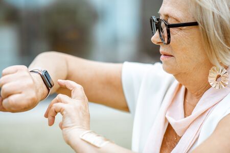 Senior woman using smart watch outdoors. Concept of using modern technologies by elderly peopleの写真素材