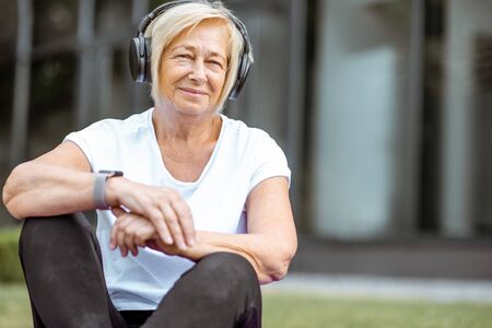 Portrait of a happy senior woman in sports clothes with headphones outdoors. Concept of a healthy lifestyle on retirementの写真素材